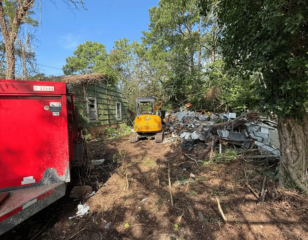 Mini excavator beside a shed demolition pile and a dump trailer on the Delmarva Peninsula
