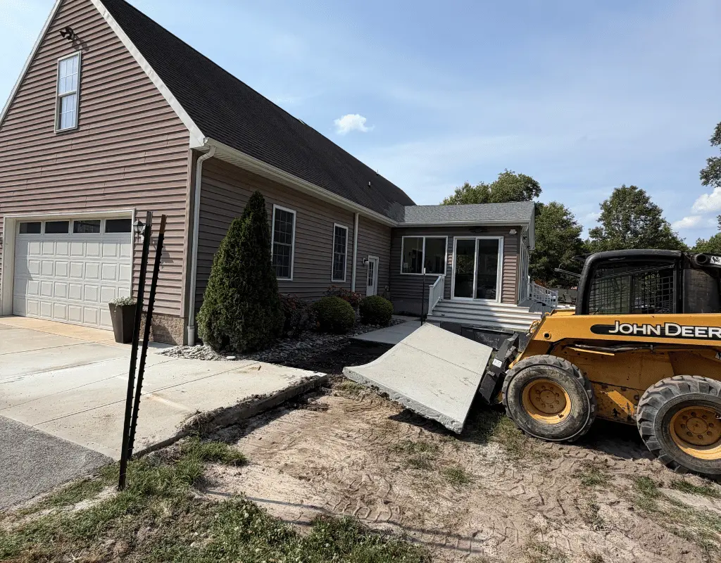 John Deere skid steer lifting a broken concrete slab beside a house on the Delmarva Peninsula