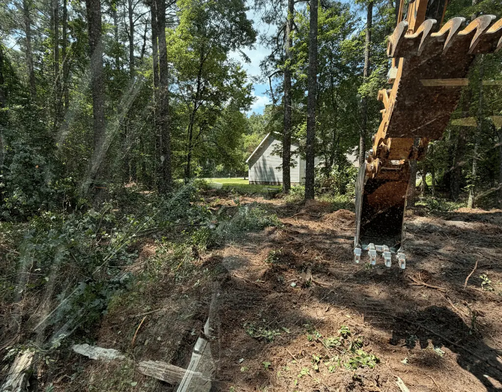 Excavator bucket over freshly cleared ground on a wooded Delmarva Peninsula lot