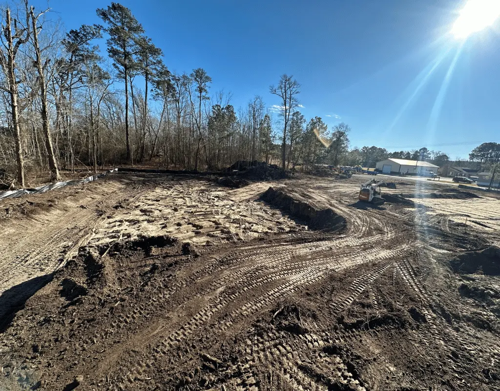 Wide cleared lot with equipment tracks and a machine working near the tree line on the Delmarva Peninsula